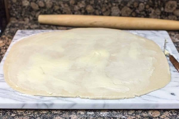 Dough for easy cinnamon rolls rolled out on a marble board with a rolling pin behind it.