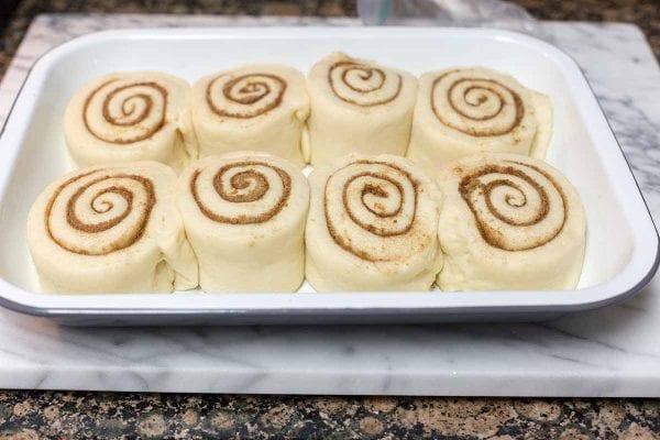 Cinnamon buns rising on a parchment lined baking sheet.