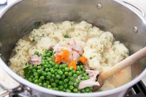 Stock pot with peas and carrots being stirred into soup with dumplings.