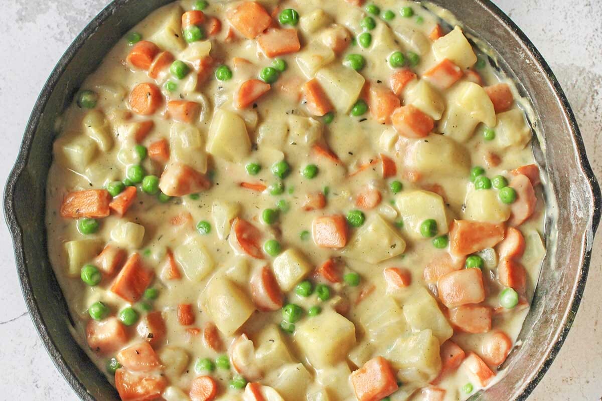 Vegetable Casserole filling with potatoes, peas and carrots in a cast iron skillet.