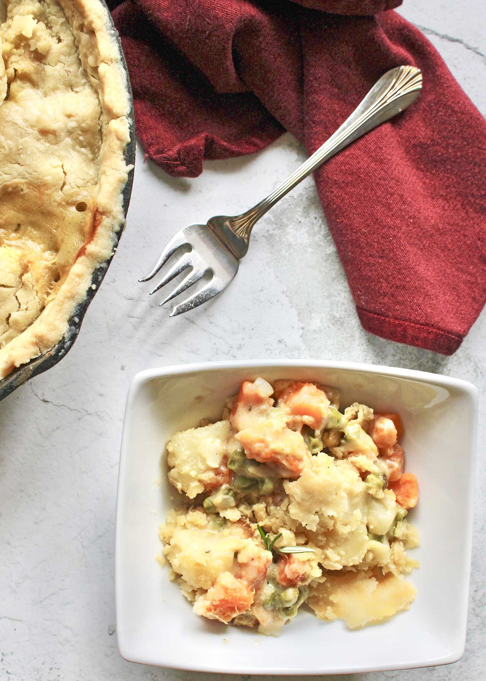 A bowl of Vegetable Casserole in a bowl with a fork and the cast iron skillet pie behind it.