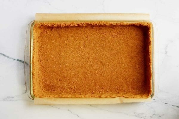 Pumpkin Pie Bars with Graham Cracker Crust pressed into a glass baking dish lined with parchment.
