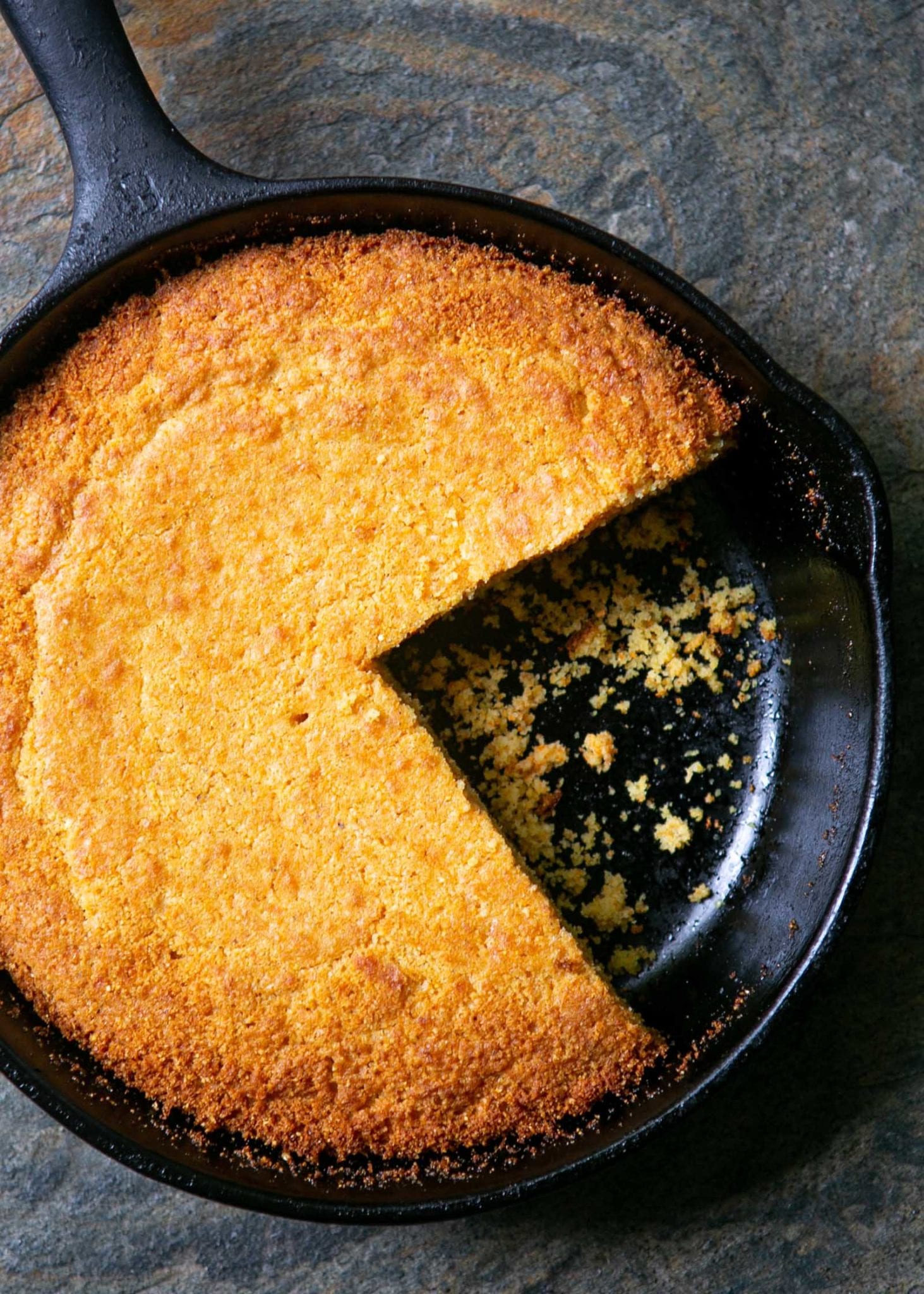 Overhead view of homemade cornbread baked in a cast iron skillet with a large slice missing.