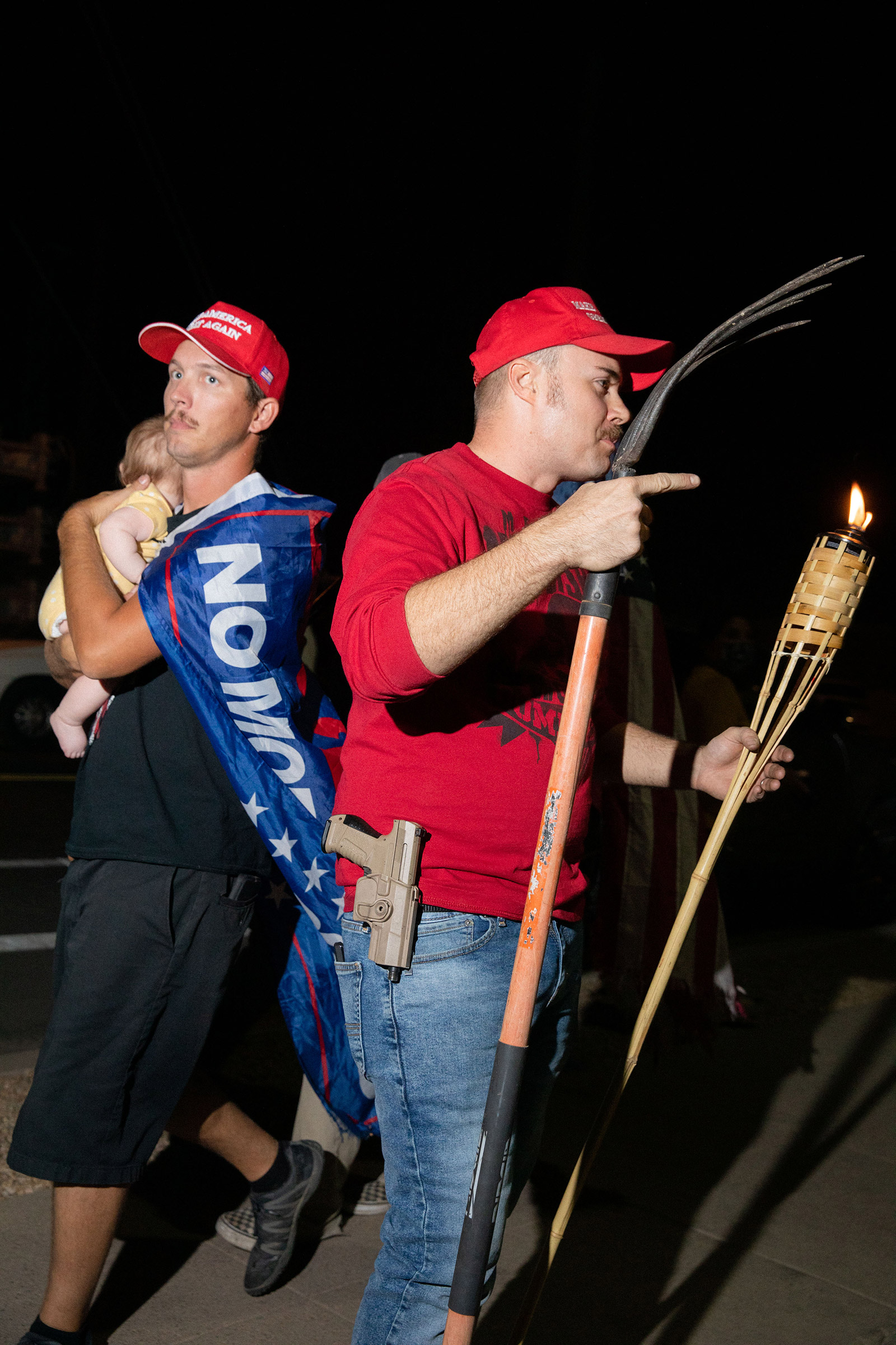A father with child walks by a man with a rake, gun and tiki torch at the Maricopa County Elections office in Phoenix, on Nov. 5, 2020.