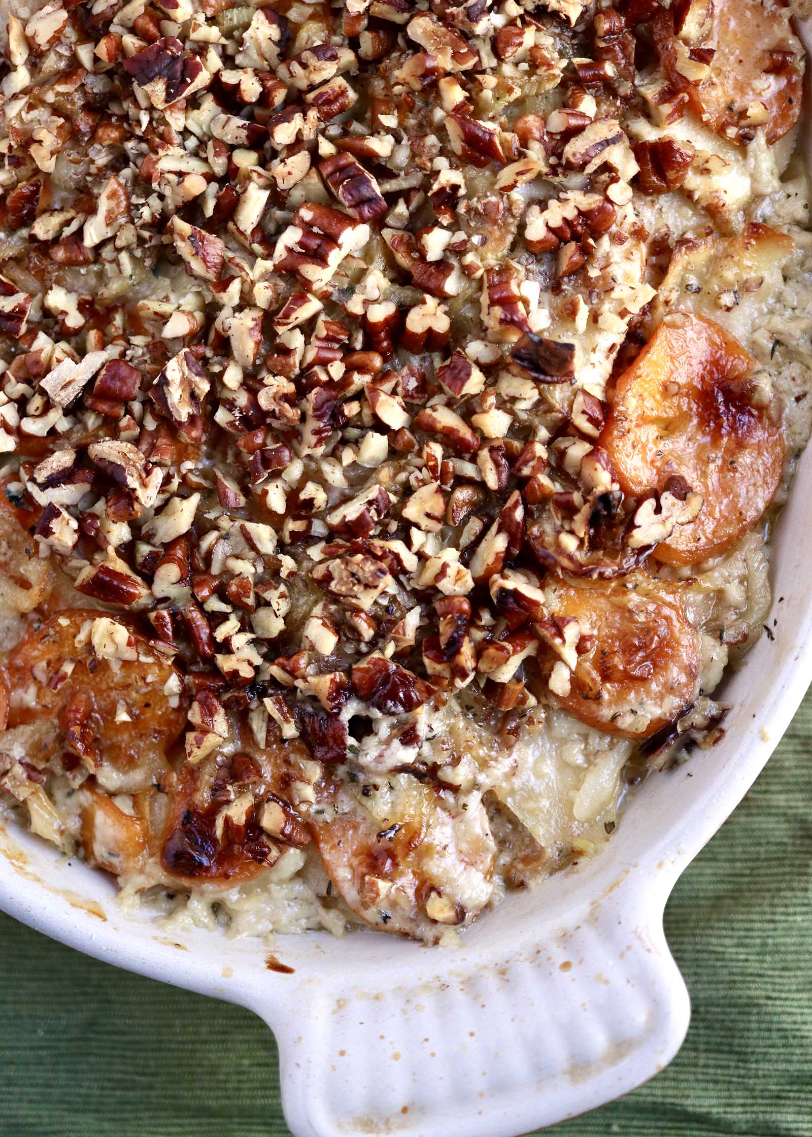 Thanksgiving Root Vegetable Gratin topped with chopped nuts and served in a casserole dish.
