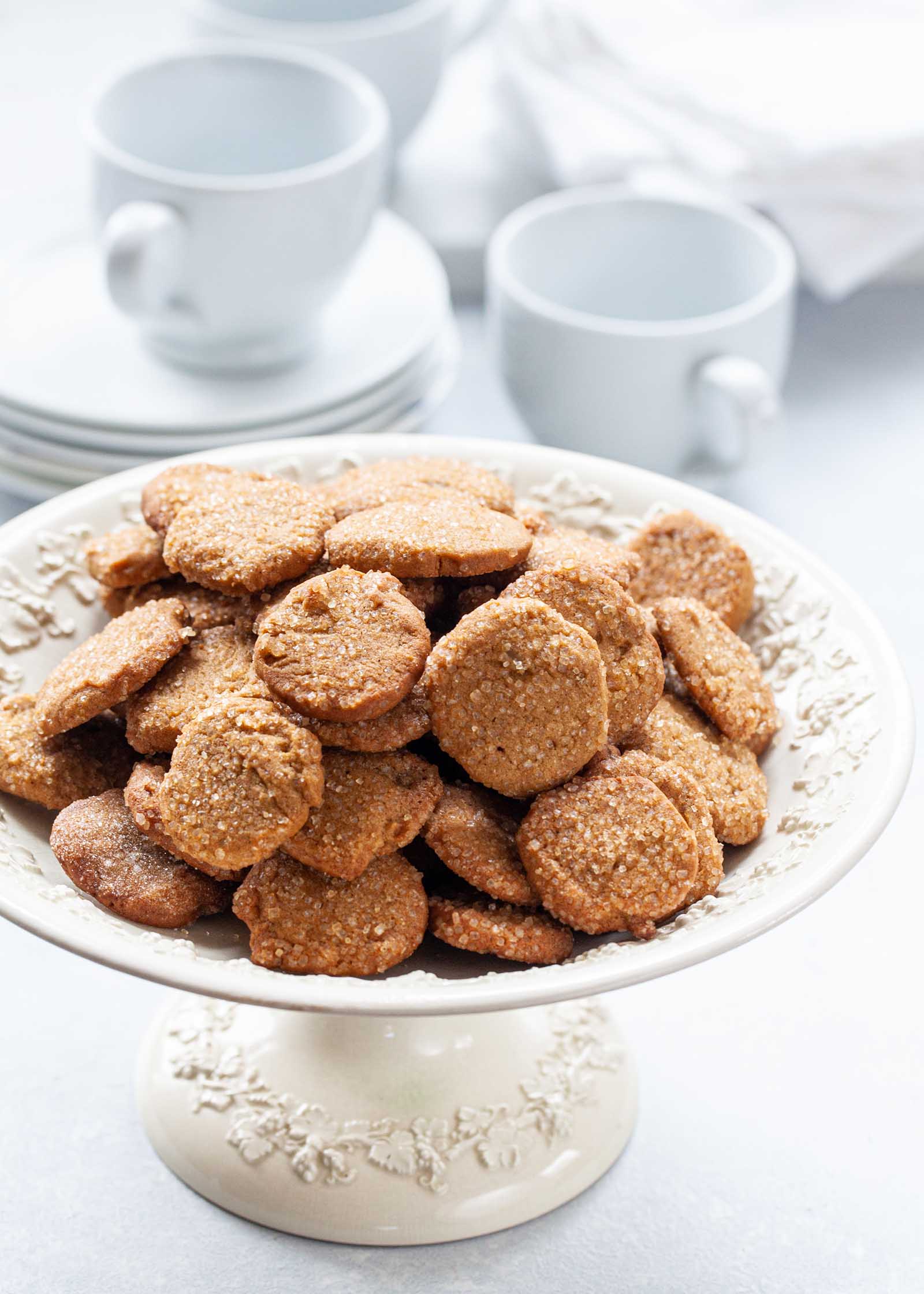 Make Ahead Slice and Bake Ginger Cookies heaped on a cake stand with coffee mugs and dessert plates set behind.