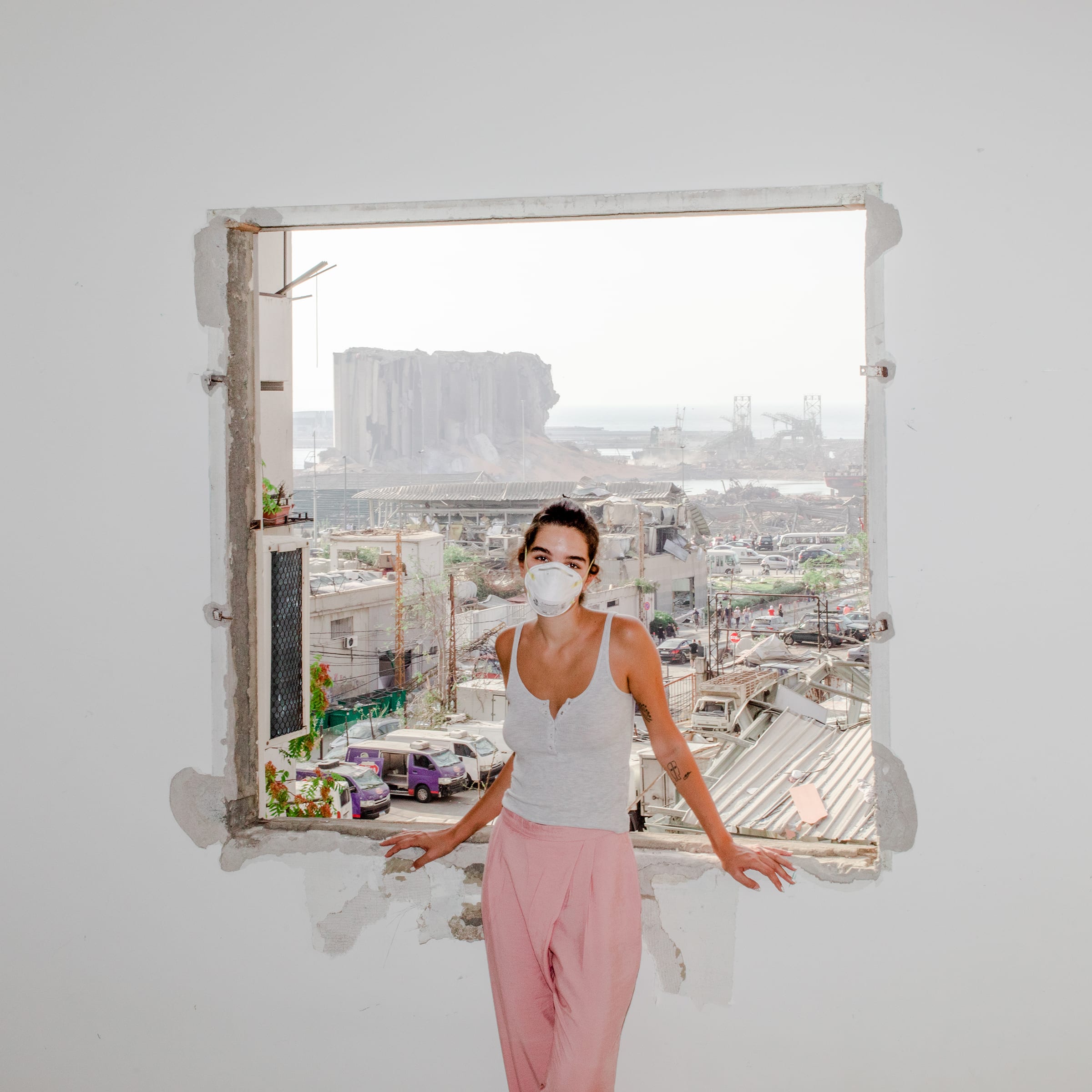Nour Saliba stands in her apartment in the Mar Mikhael area of Beirut on Aug. 6, two days after the deadly explosion at the city’s port, seen through her blown-out window.  After the Explosion,  Aug. 31 issue.