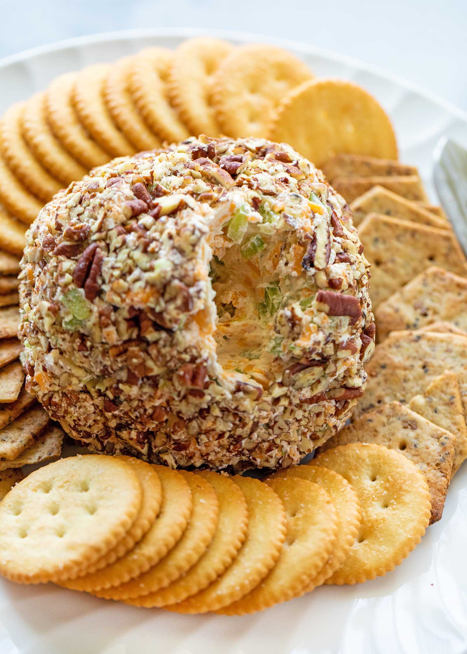A homemade cheese ball is pictured with some scooped out. Crackers are all around the cheese ball.