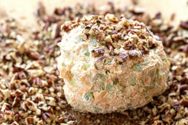 A cheese ball is being covered with chopped nuts to show how to make a cheese ball.