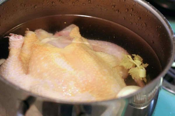 A whole chicken in a large stockpot with water to make a chicken pot pie casserole.