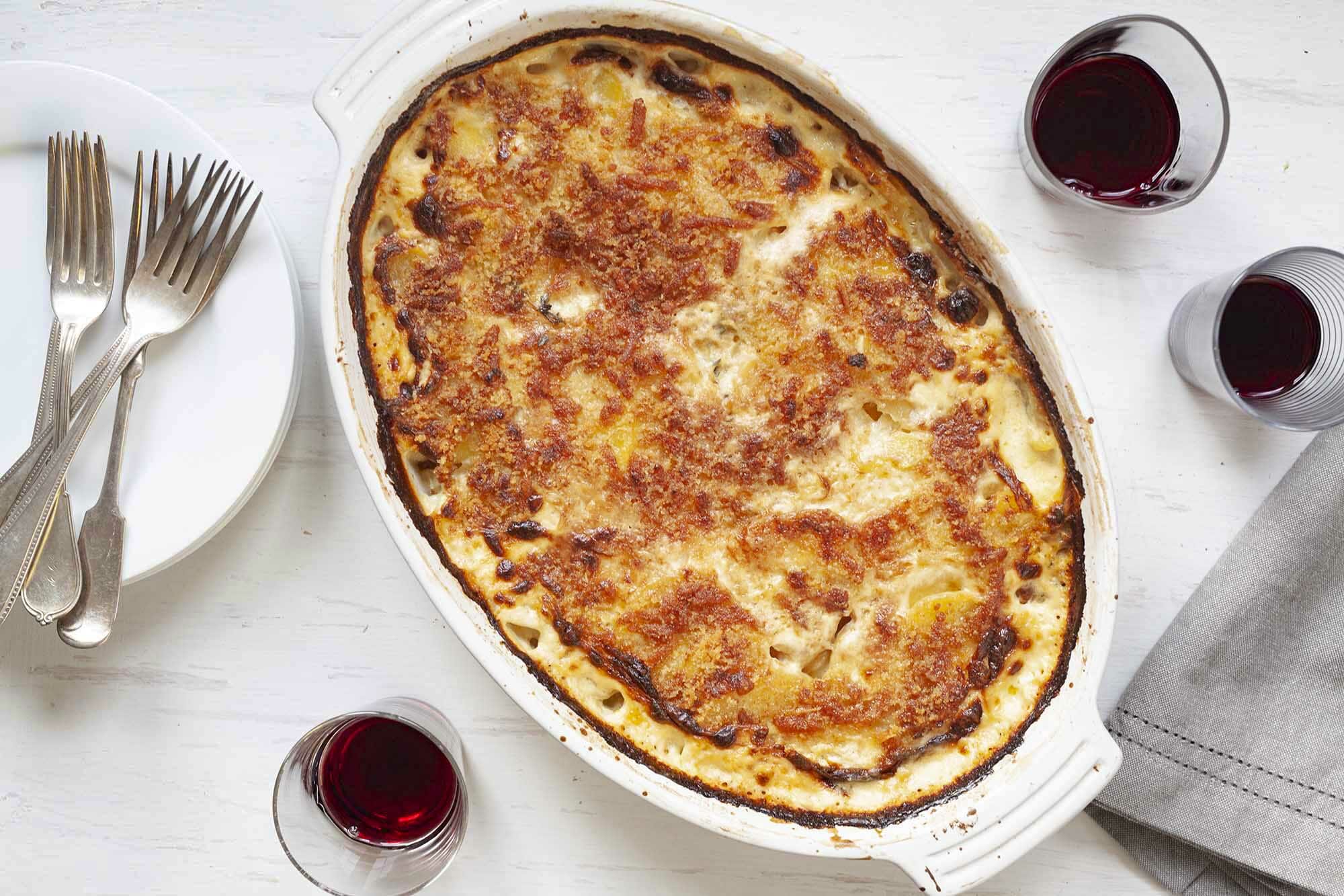 EAsy Au Gratin baked in an oval casserole dish and surrounded by small glasses of red wine, forks and plates.