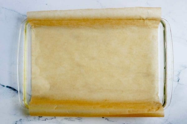 A baking dish lined with parchment paper to show how to make Pumpkin Pie Bars.