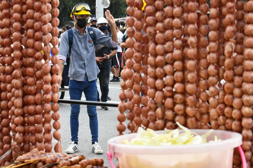 In this file photo taken October 21, 2020, a pro-democracy protesters gestures near a street food vendor selling grilled sausages during an anti-government rally in Bangkok. — AFP pic